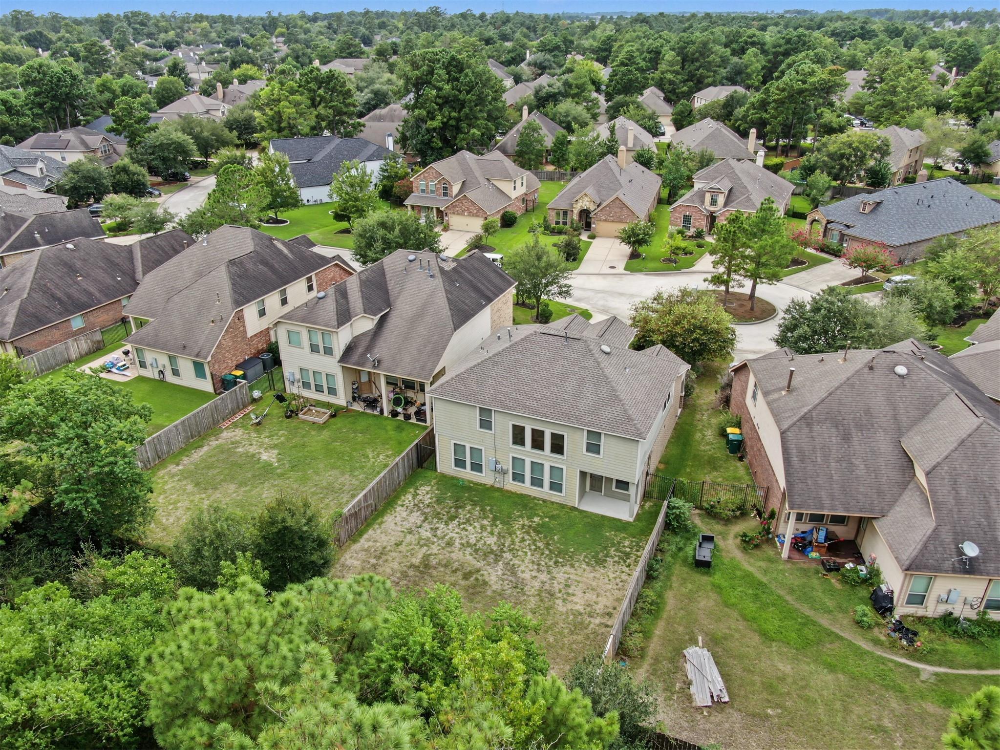 Aerial view of a two-story home with a fenced backyard among leafy suburban homes.