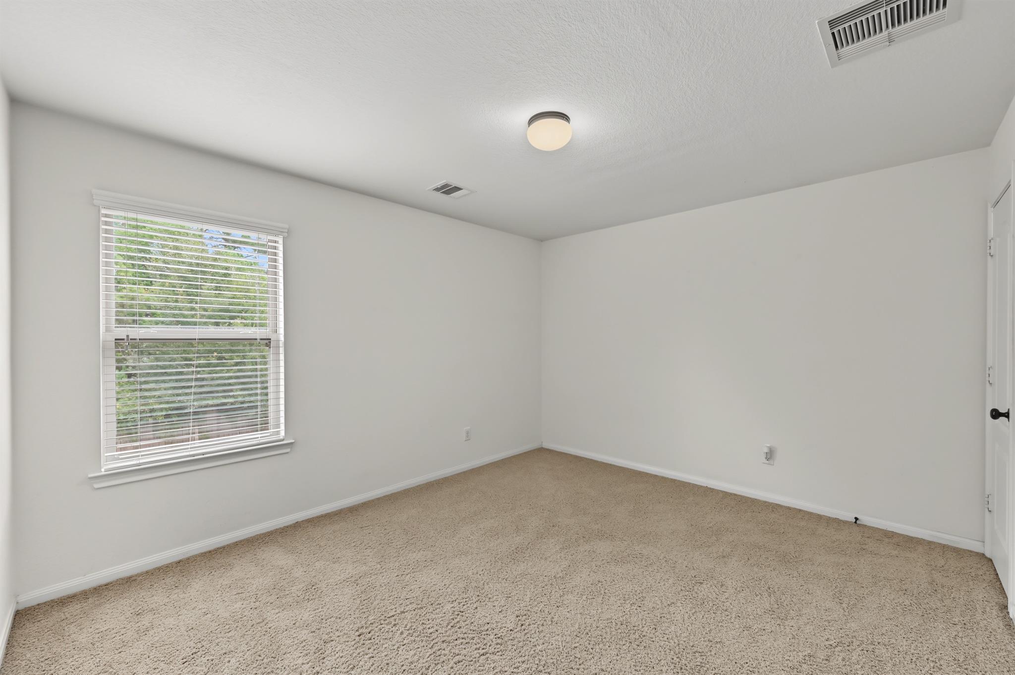 Empty bedroom with beige carpet and a window fitted with white blinds.