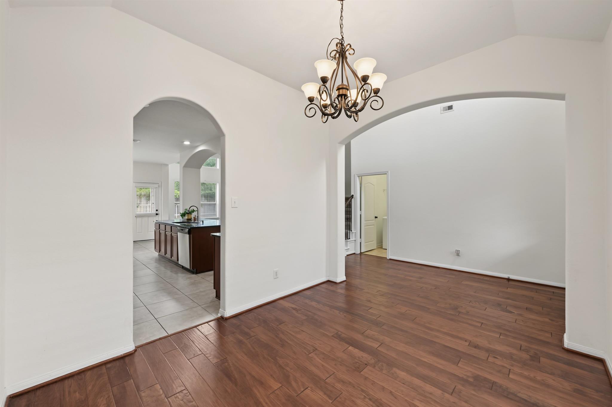 Dining area with wood floors, a bronze chandelier, and arched openings to the kitchen and hallway.