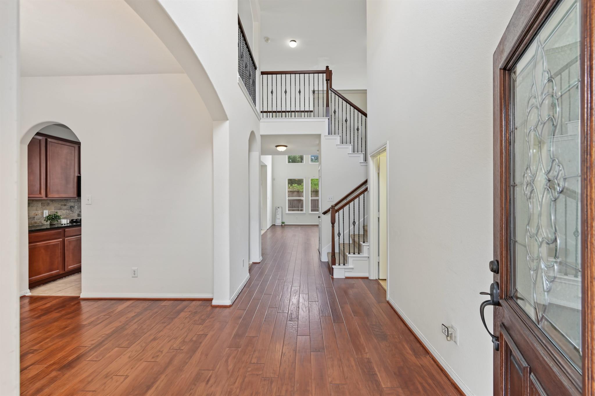 Unfurnished entry foyer with wood floors, a decorative glass front door, and a staircase with dark railings.