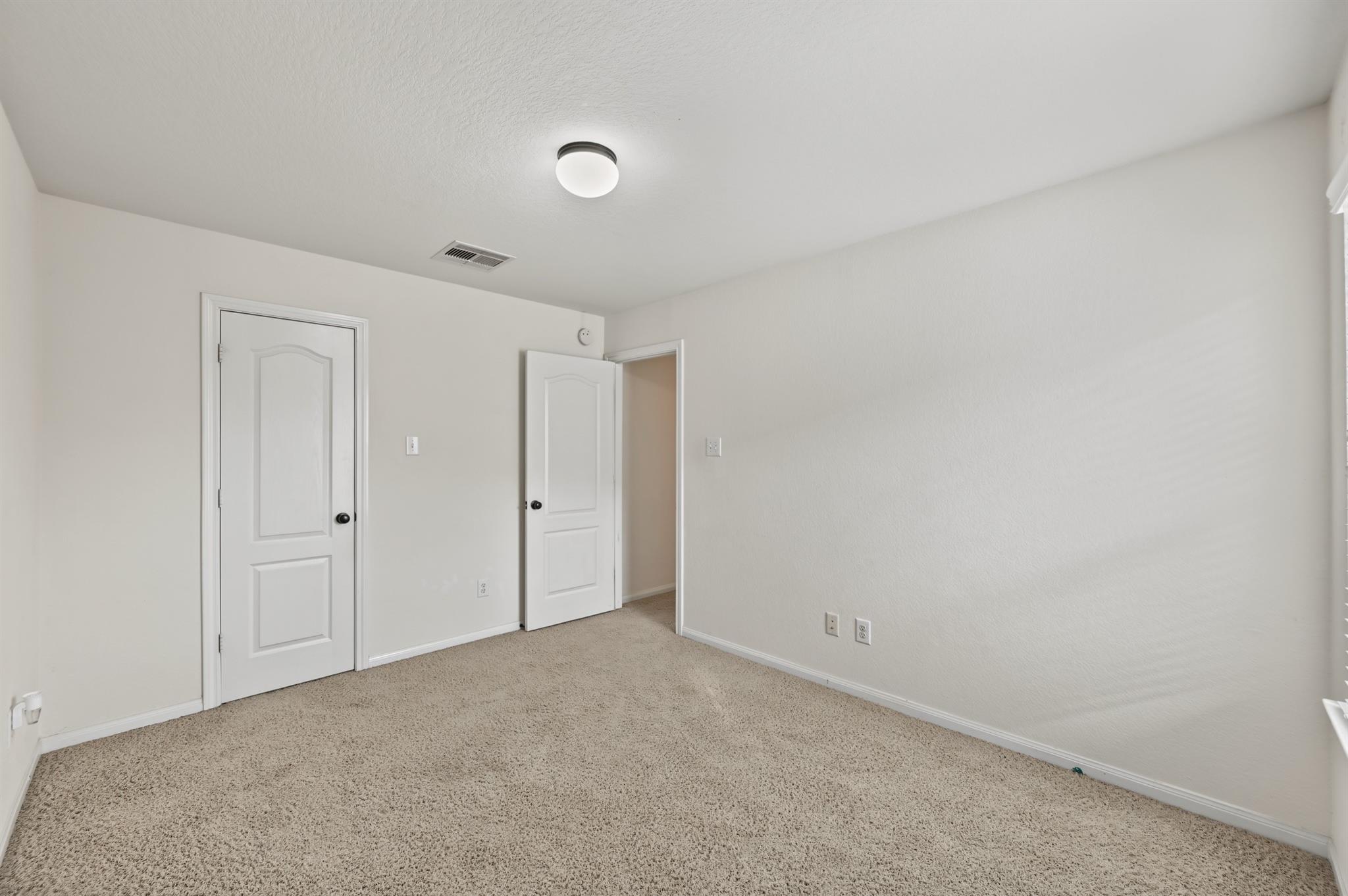 Empty carpeted room with white walls and two doors.