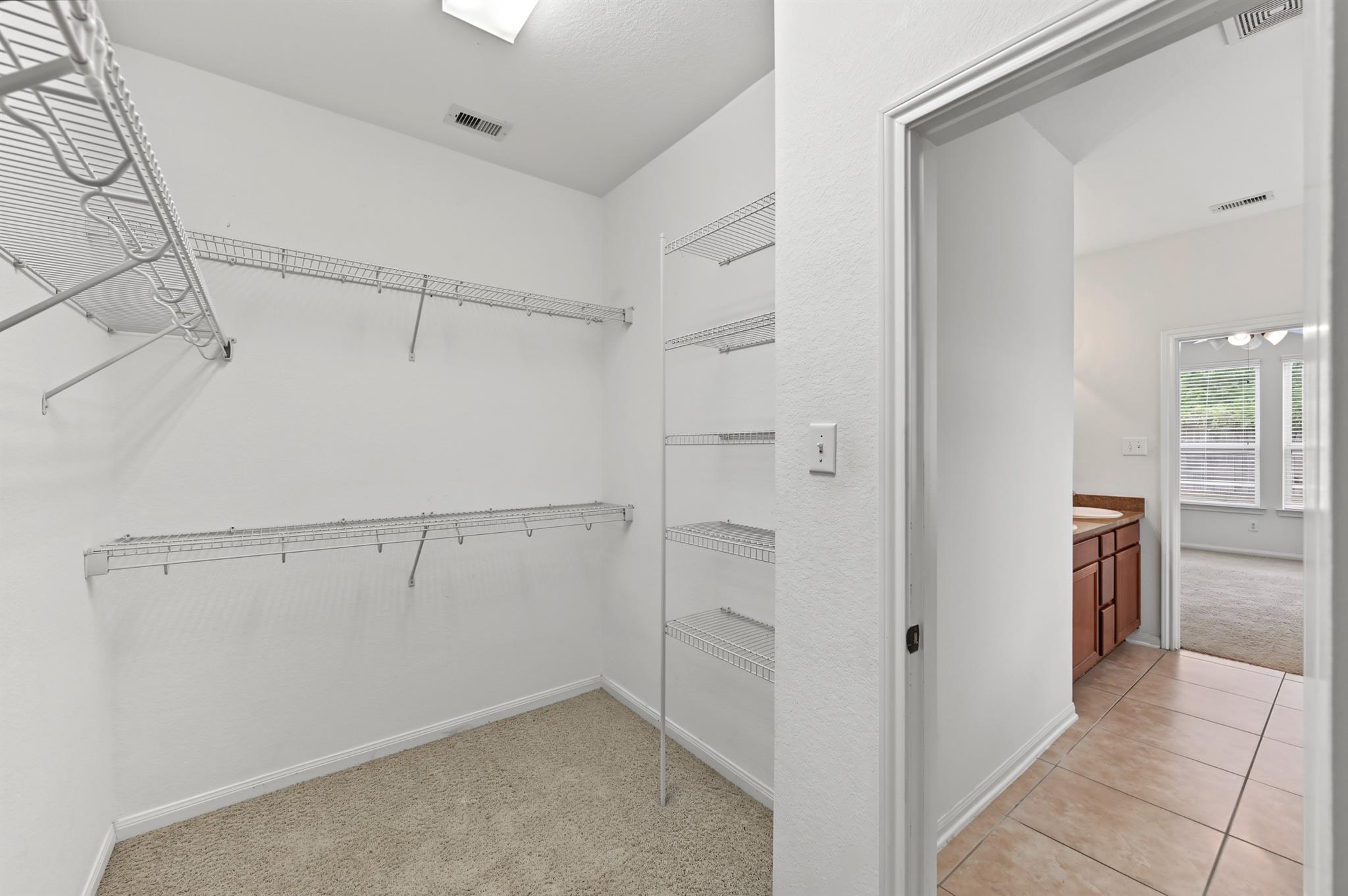 Walk-in closet with white wire shelving and carpet, opening onto a tiled bathroom.
