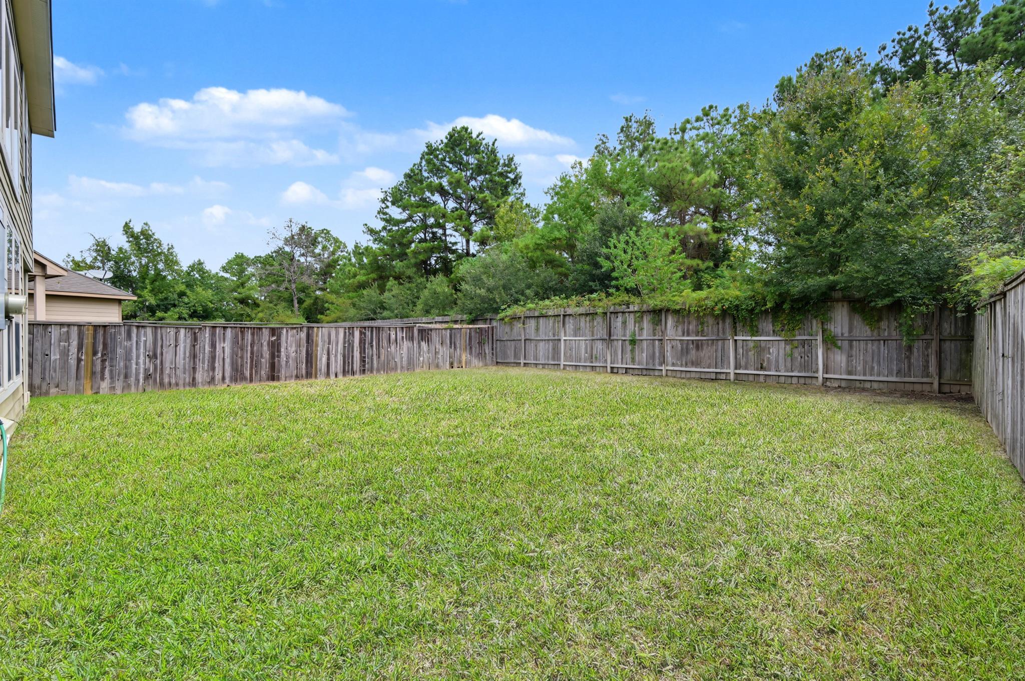 Grassy backyard enclosed by a wooden privacy fence, with mature trees beyond.