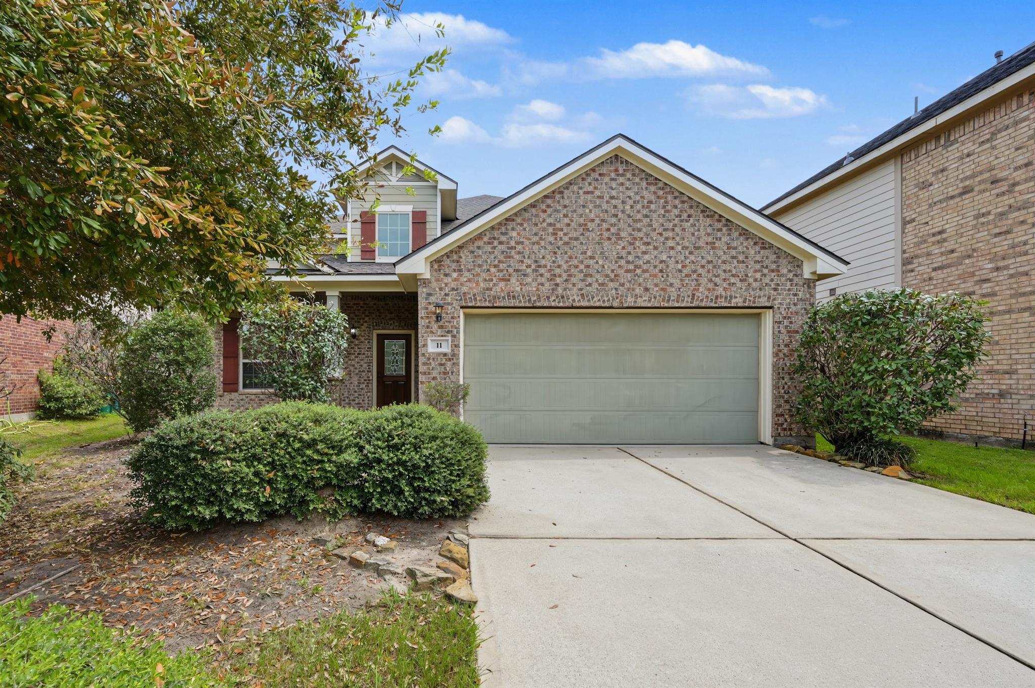 Brick-front house with a wide garage, concrete driveway, and landscaped shrubs.