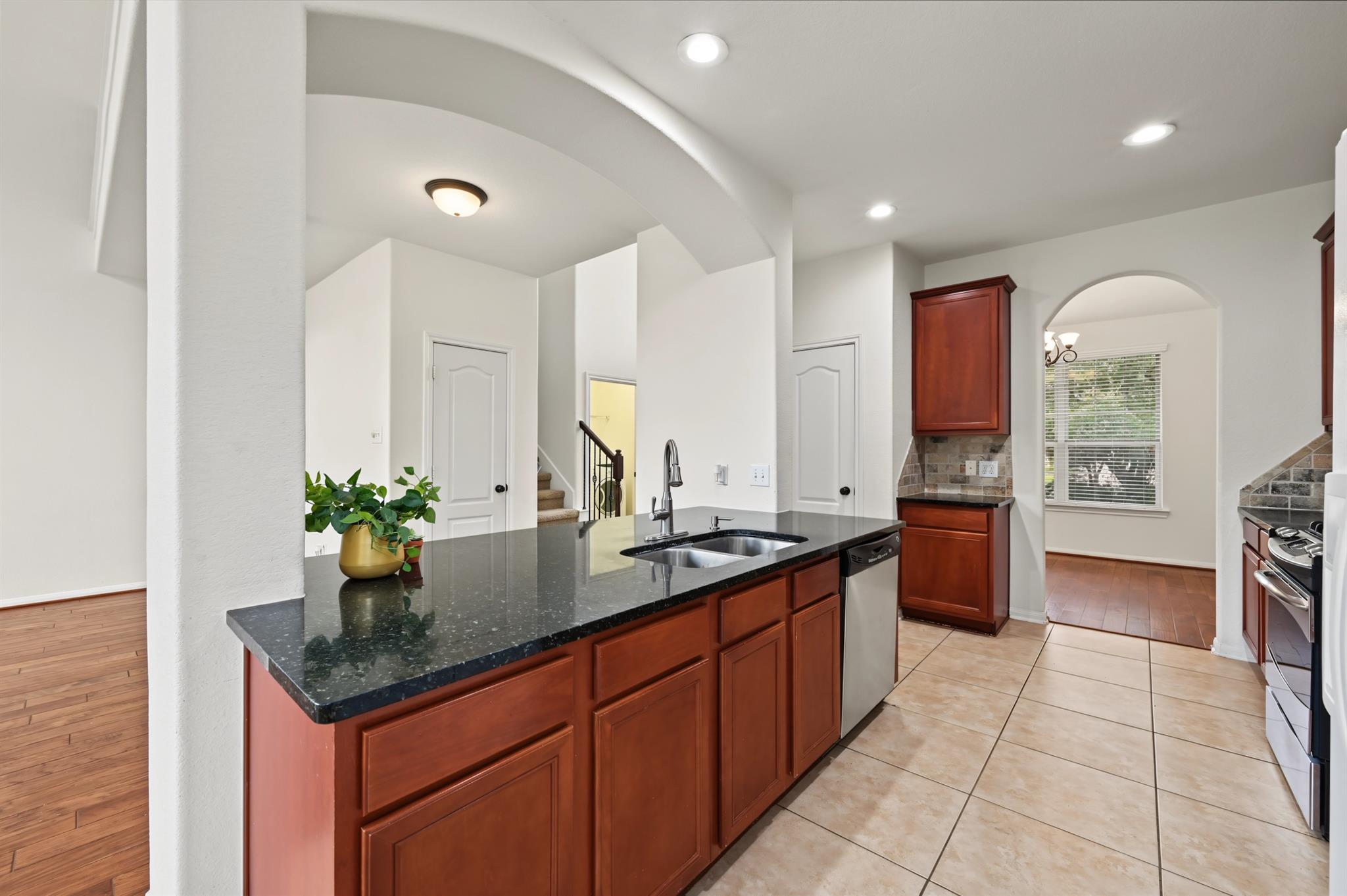 Kitchen with a dark granite island, double sink, reddish wood cabinets, and an arched opening to the dining area.