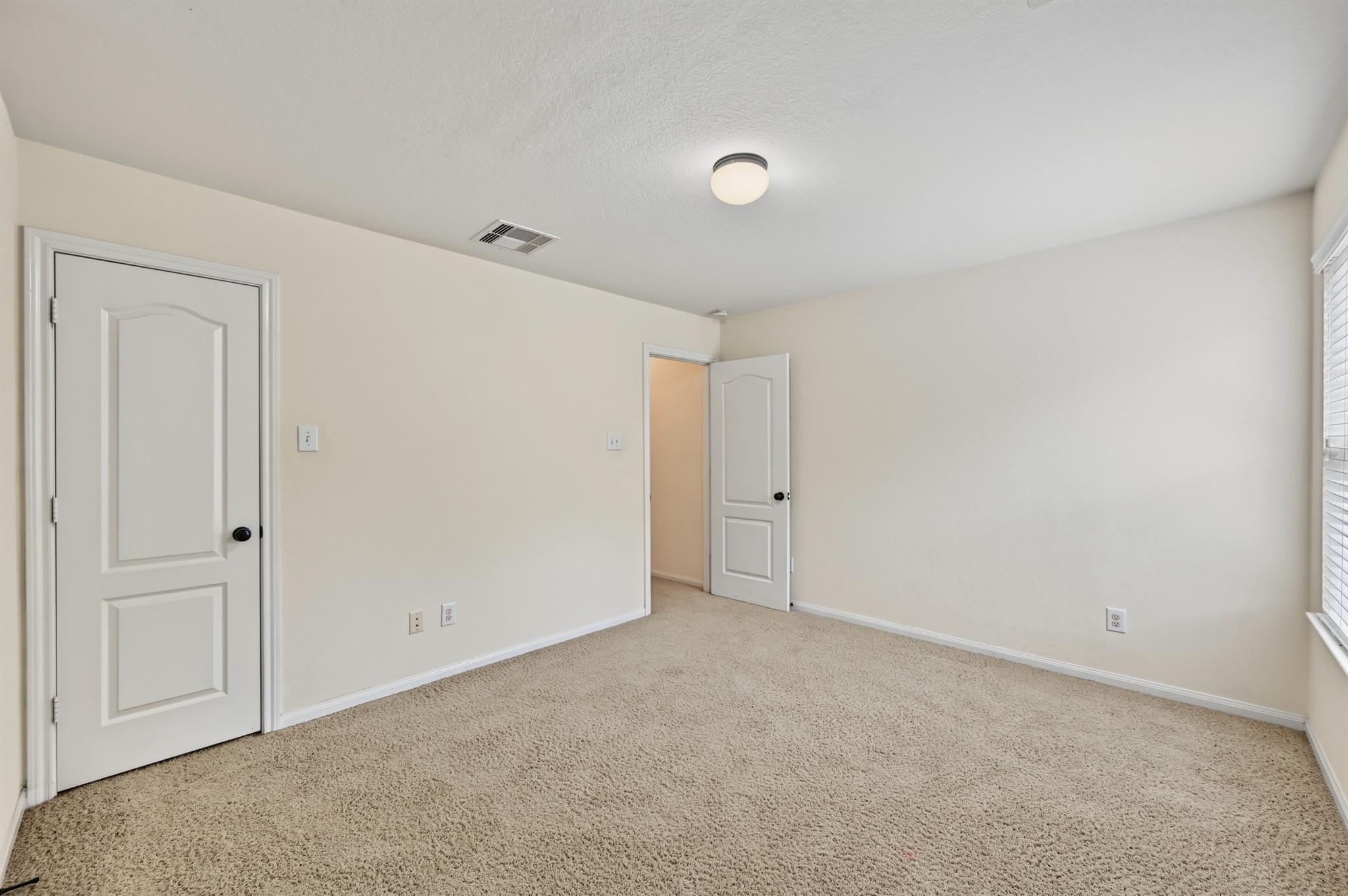 Empty carpeted room with cream walls, two white doors, and a window with blinds.