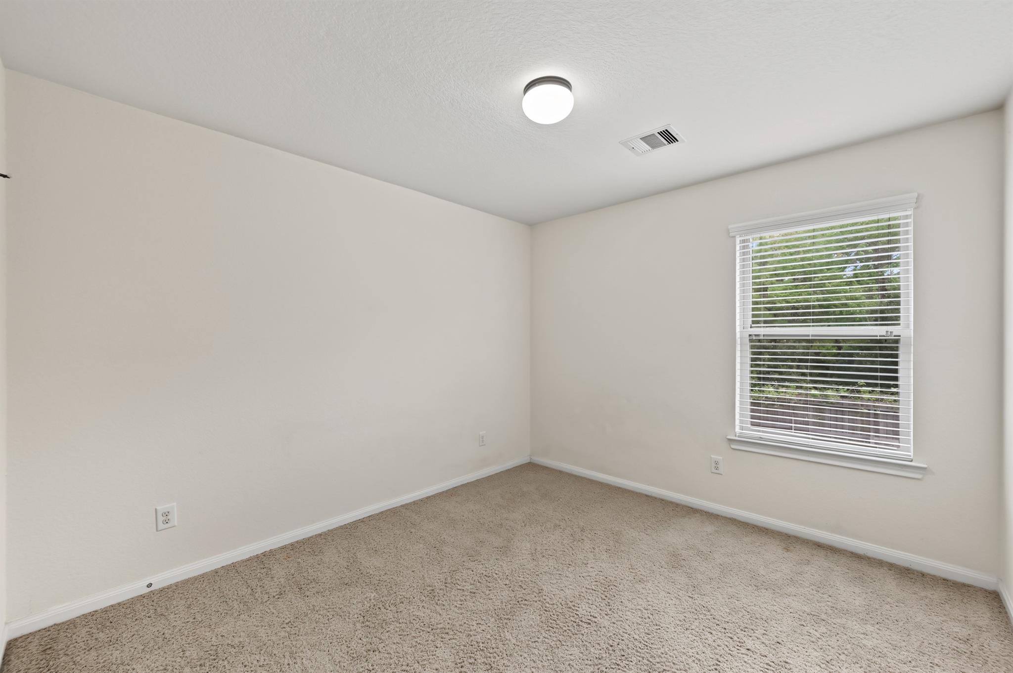 Empty carpeted bedroom with a window fitted with white blinds.