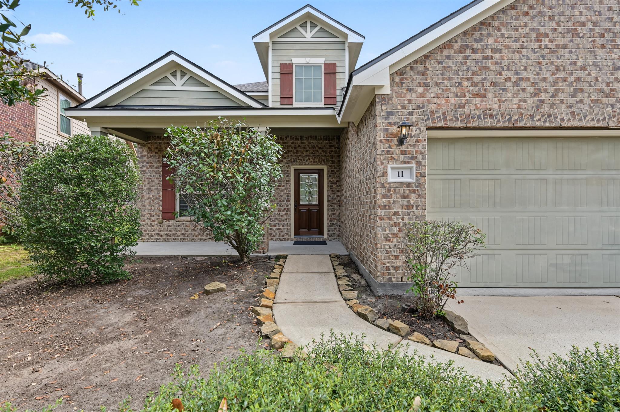 Brick-front home with covered entry, attached garage, and curved stone-edged walkway.