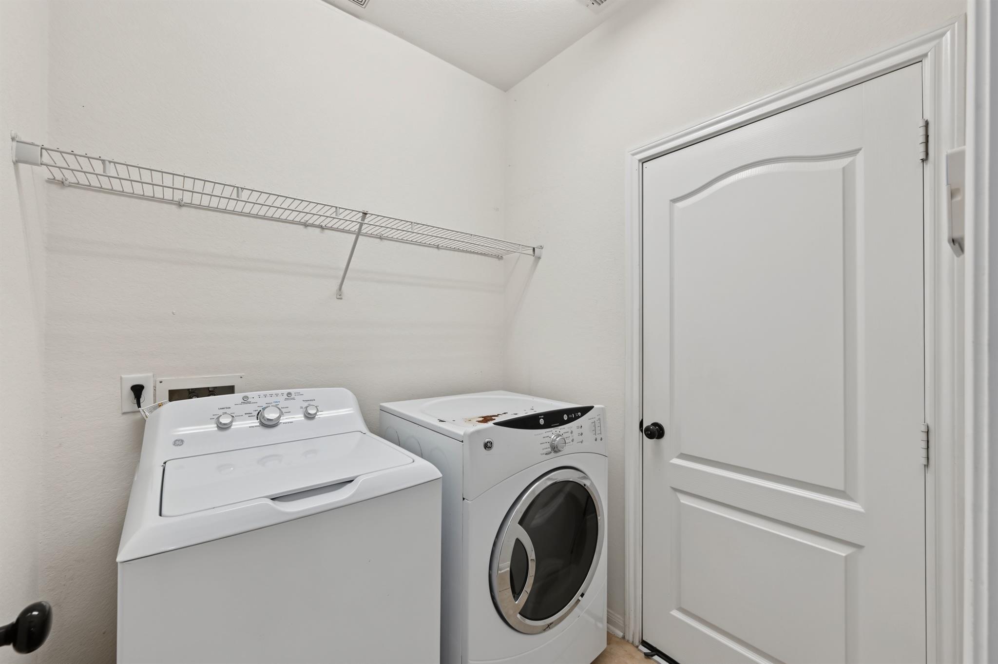 Laundry room with a top-load washer, front-load dryer, and long wire shelf.