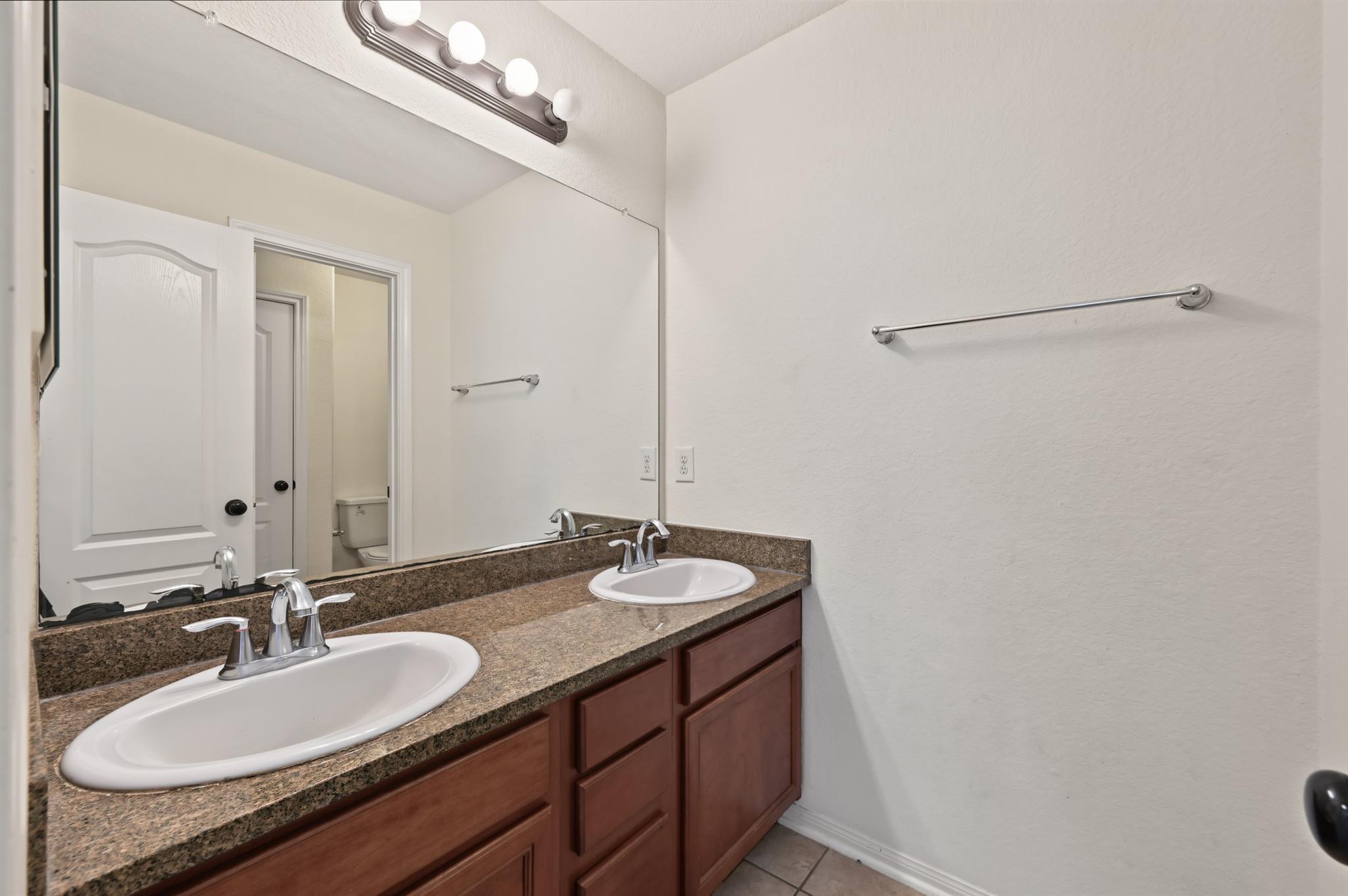 Bathroom vanity with two sinks, a speckled granite counter, and reddish-brown cabinets.