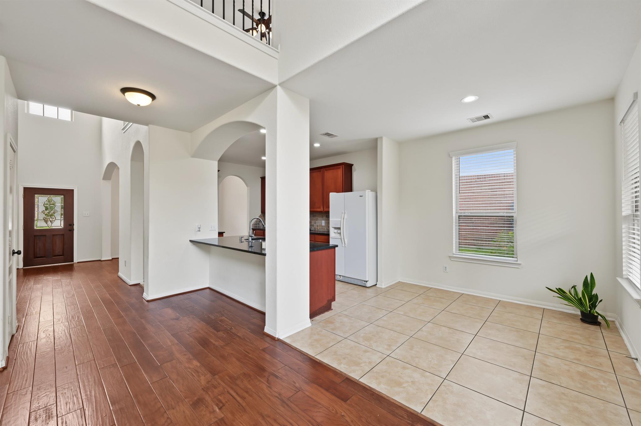 Open entry and kitchen with arched openings, reddish wood flooring, tile, and reddish cabinets.