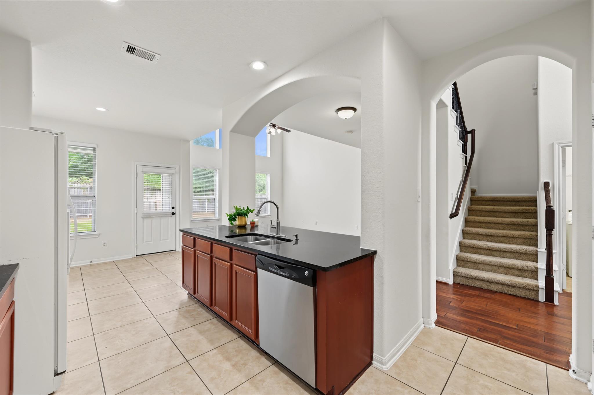 Kitchen with black countertops and reddish cabinets beside an arched opening to a carpeted staircase.
