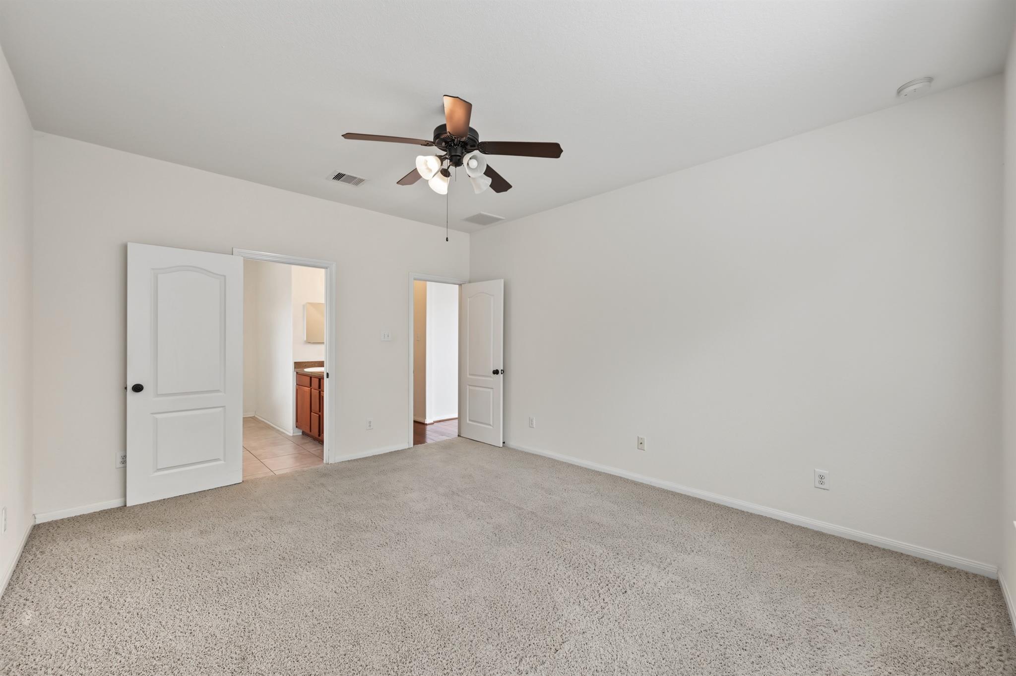 Empty carpeted bedroom with a dark ceiling fan and open doors to adjoining rooms.