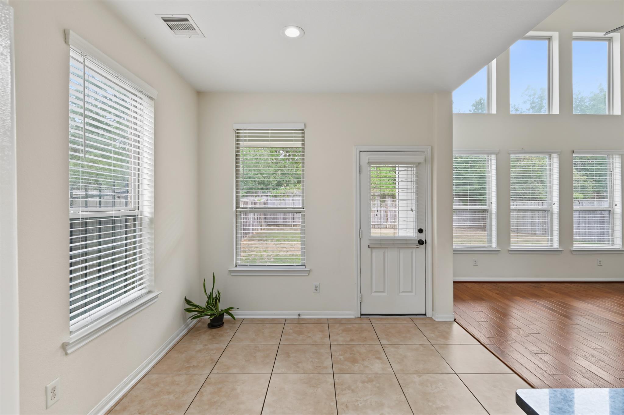 Tiled entry with a white exterior door and abundant windows, opening to a hardwood-floored room.
