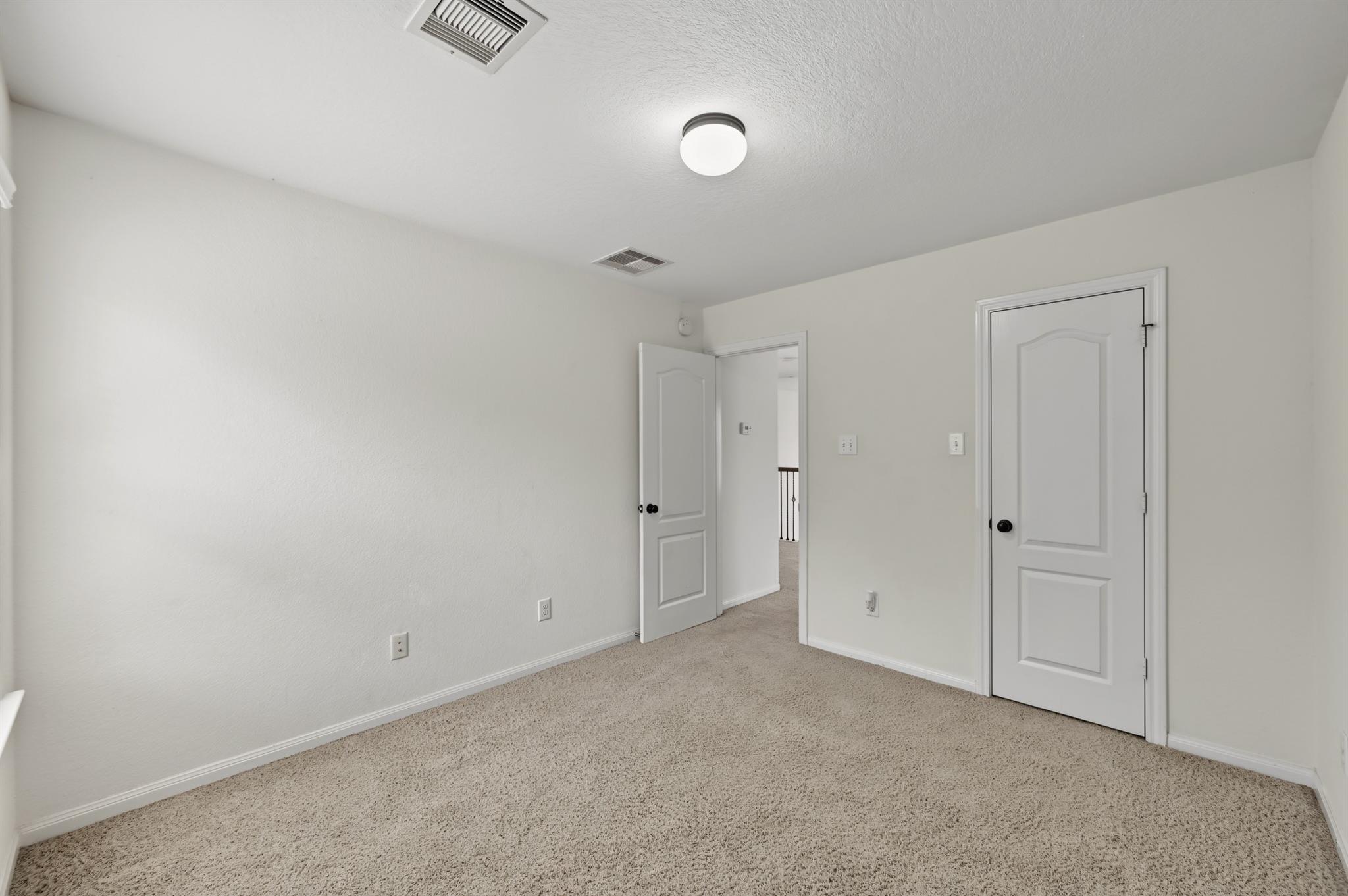 Empty carpeted bedroom with white walls, two paneled doors, and a ceiling light.