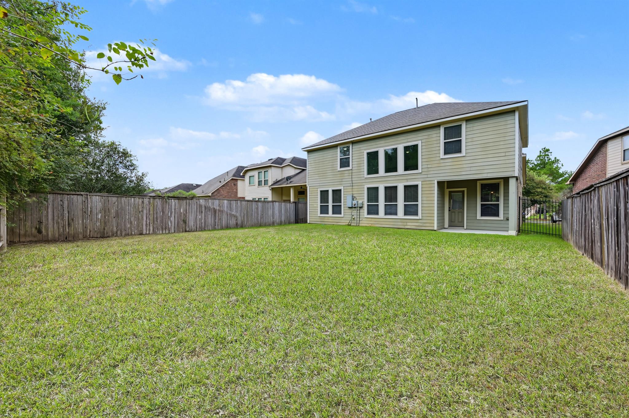 Two-story house behind a broad grassy backyard enclosed by wooden fencing.