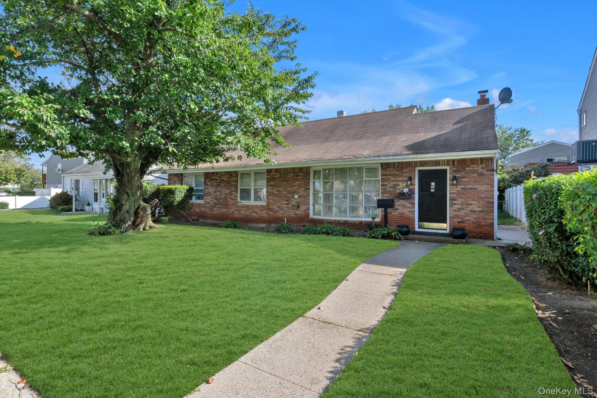 Single-story brick house with a broad lawn, curved walkway, and large shade tree.