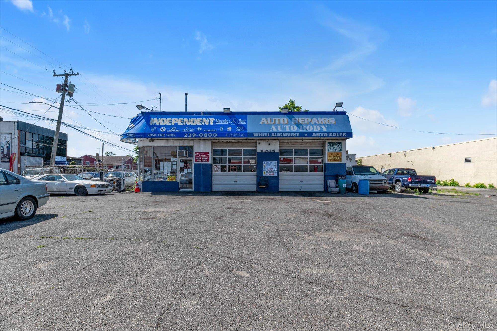 Blue-and-white auto repair shop with parked vehicles and a broad asphalt lot.