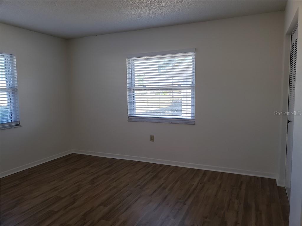 Unfurnished room with wood-look flooring, two windows with blinds, and a closet door.