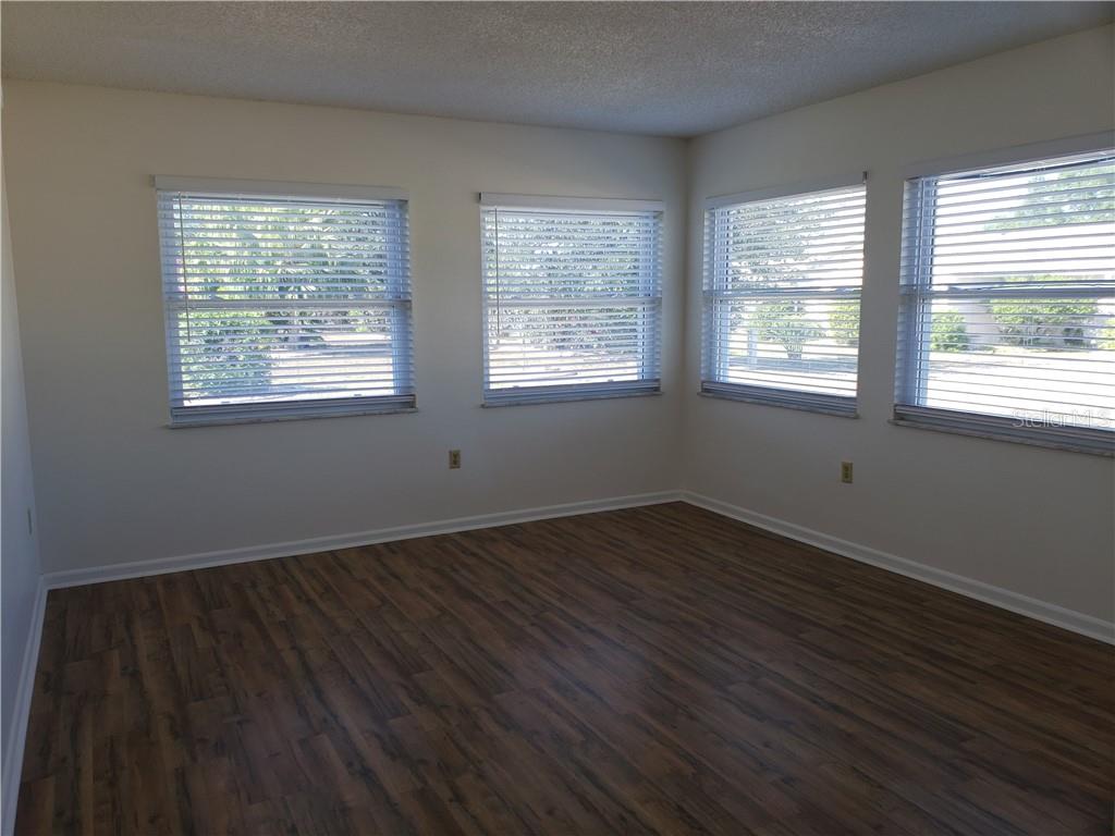 Empty room with four blinded windows and dark wood-look plank flooring.