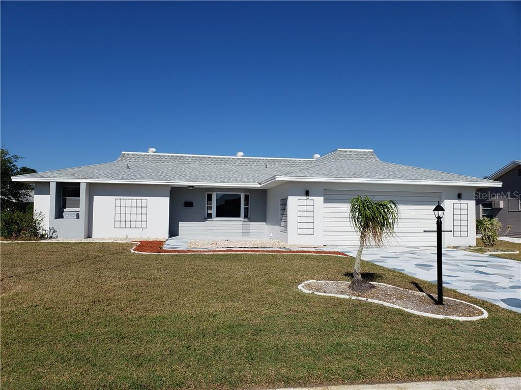 Single-story gray home with an attached garage, patterned driveway, and small palm tree.