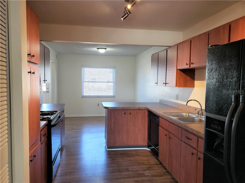 Kitchen with reddish wood cabinets, a peninsula, double sink, and black appliances.