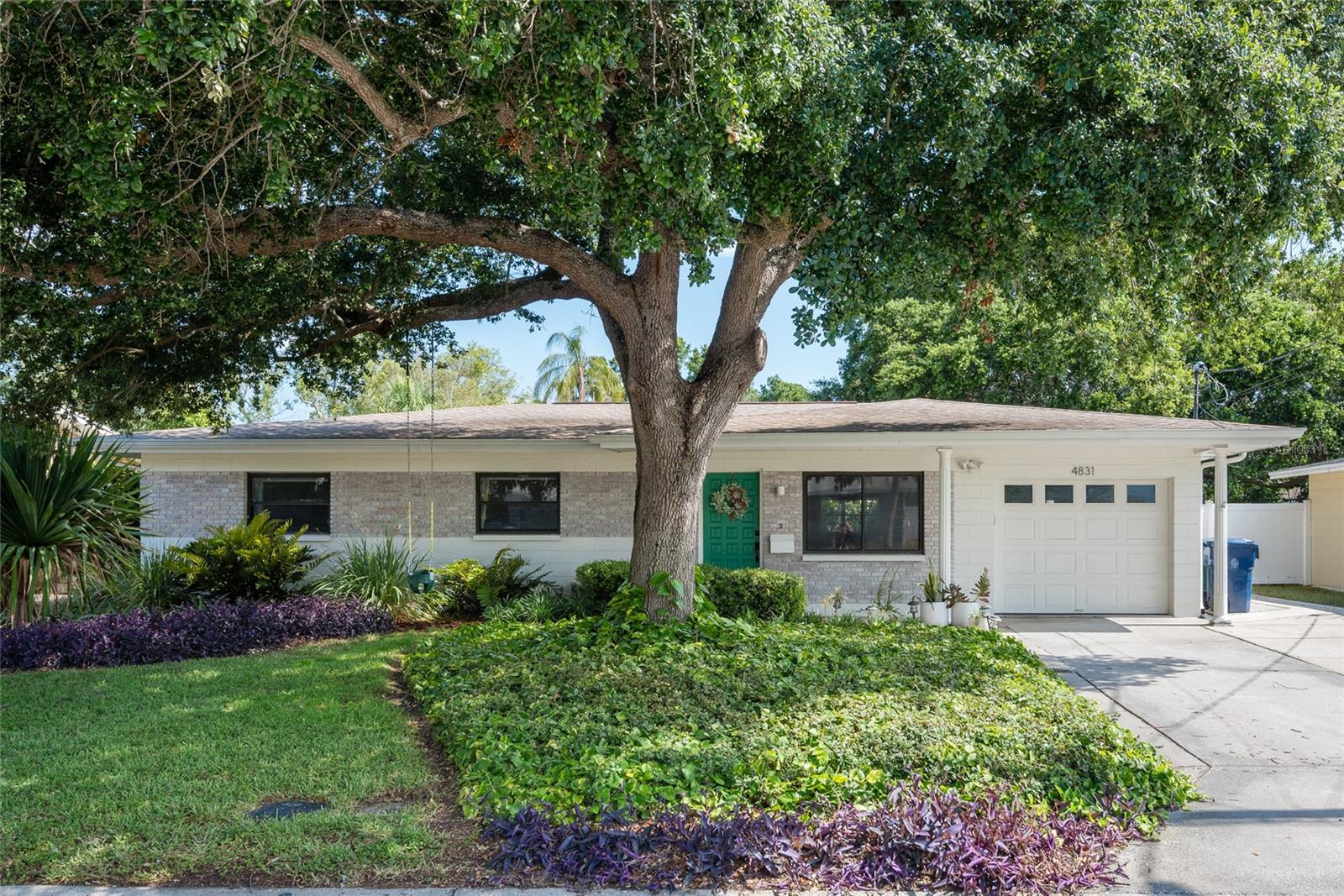 Single-story home with a green front door, attached garage, and large shade tree.