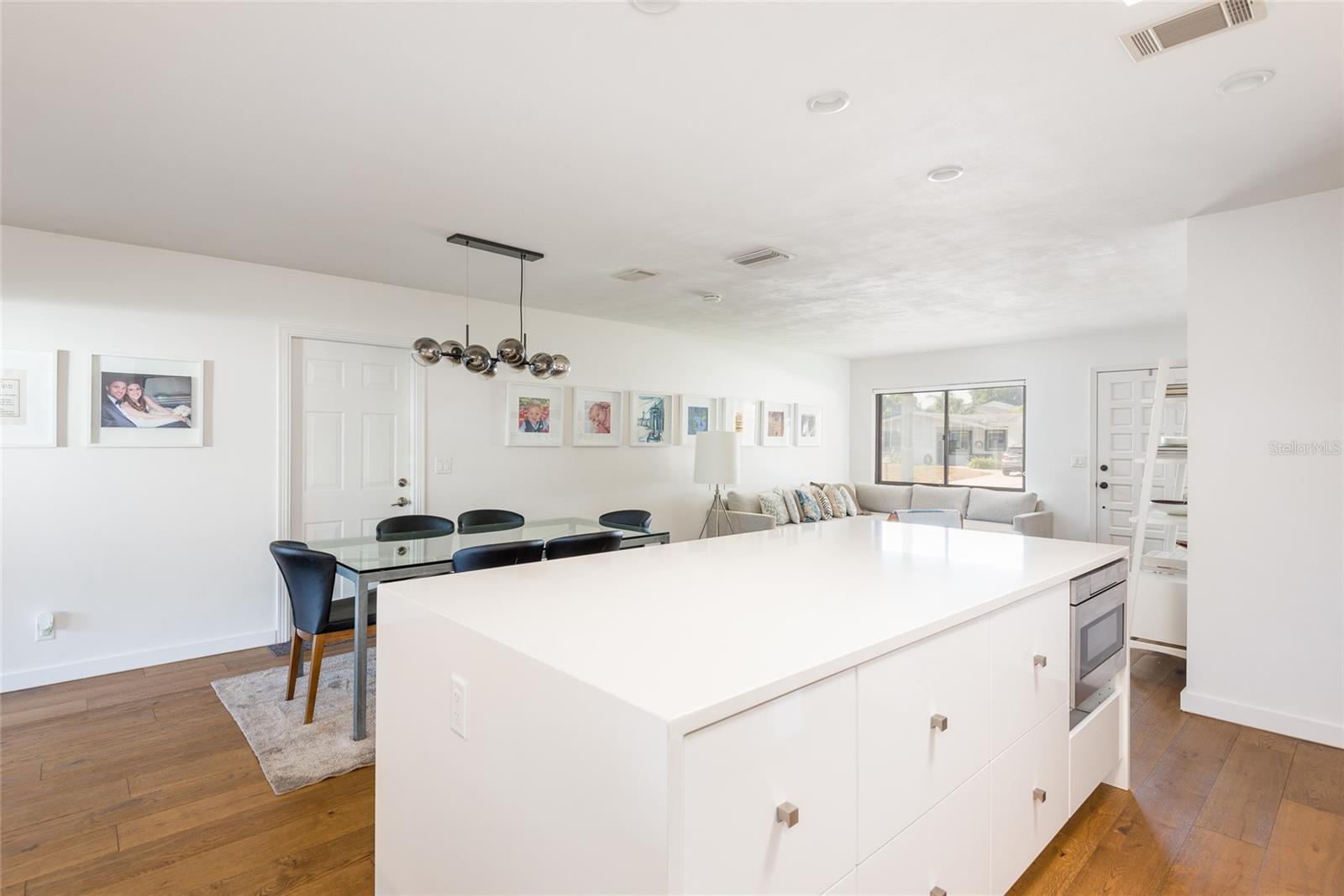 Open-plan kitchen with a large white island, glass dining table, and adjoining living room.