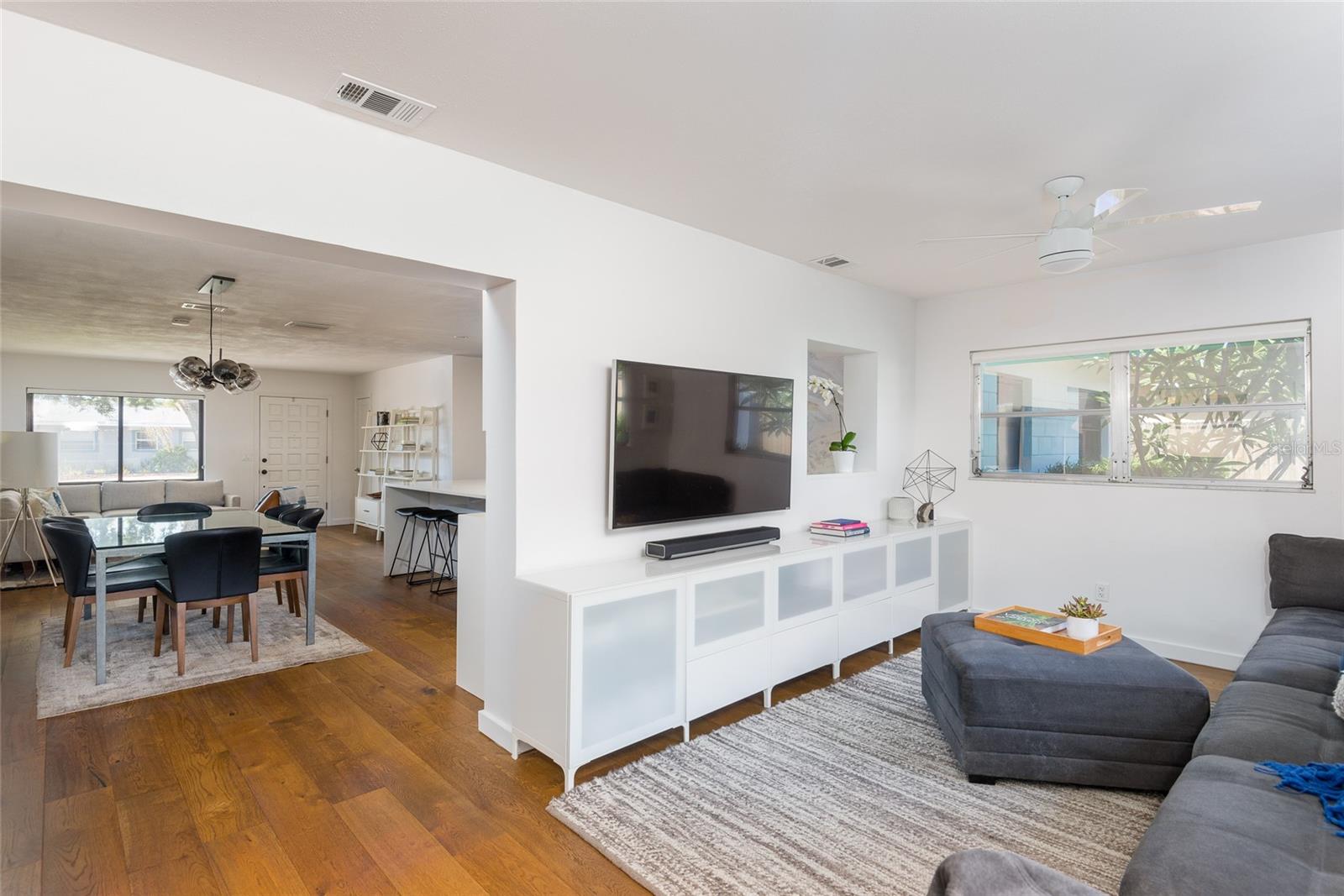 Open-plan living and dining area with wood floors, gray sectional, and wall-mounted television.