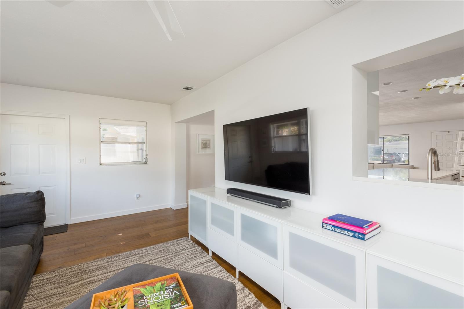 Living room with a wall-mounted television, white media cabinet, gray sofa, and wood floors.