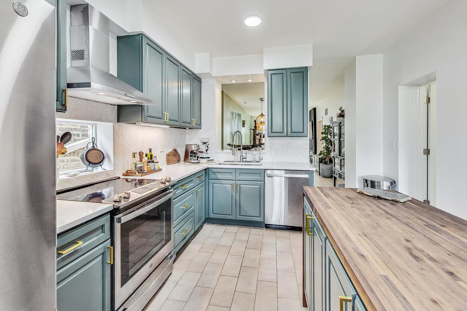 Kitchen with blue-green cabinets, stainless appliances, and a large butcher-block island.