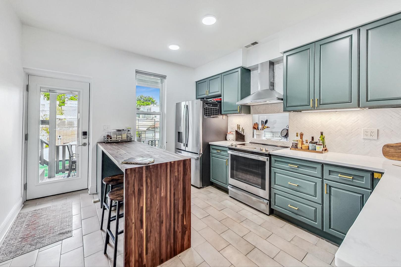 Kitchen with teal cabinets, stainless appliances, and a wood-paneled island beside a glass deck door.