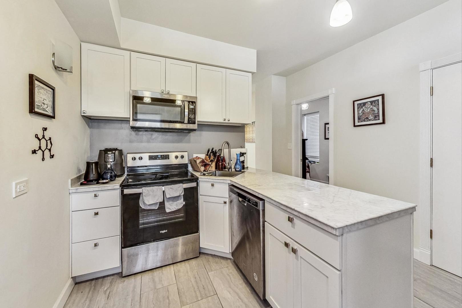 Kitchen with white cabinets, stainless steel appliances, and a long marble-look peninsula.