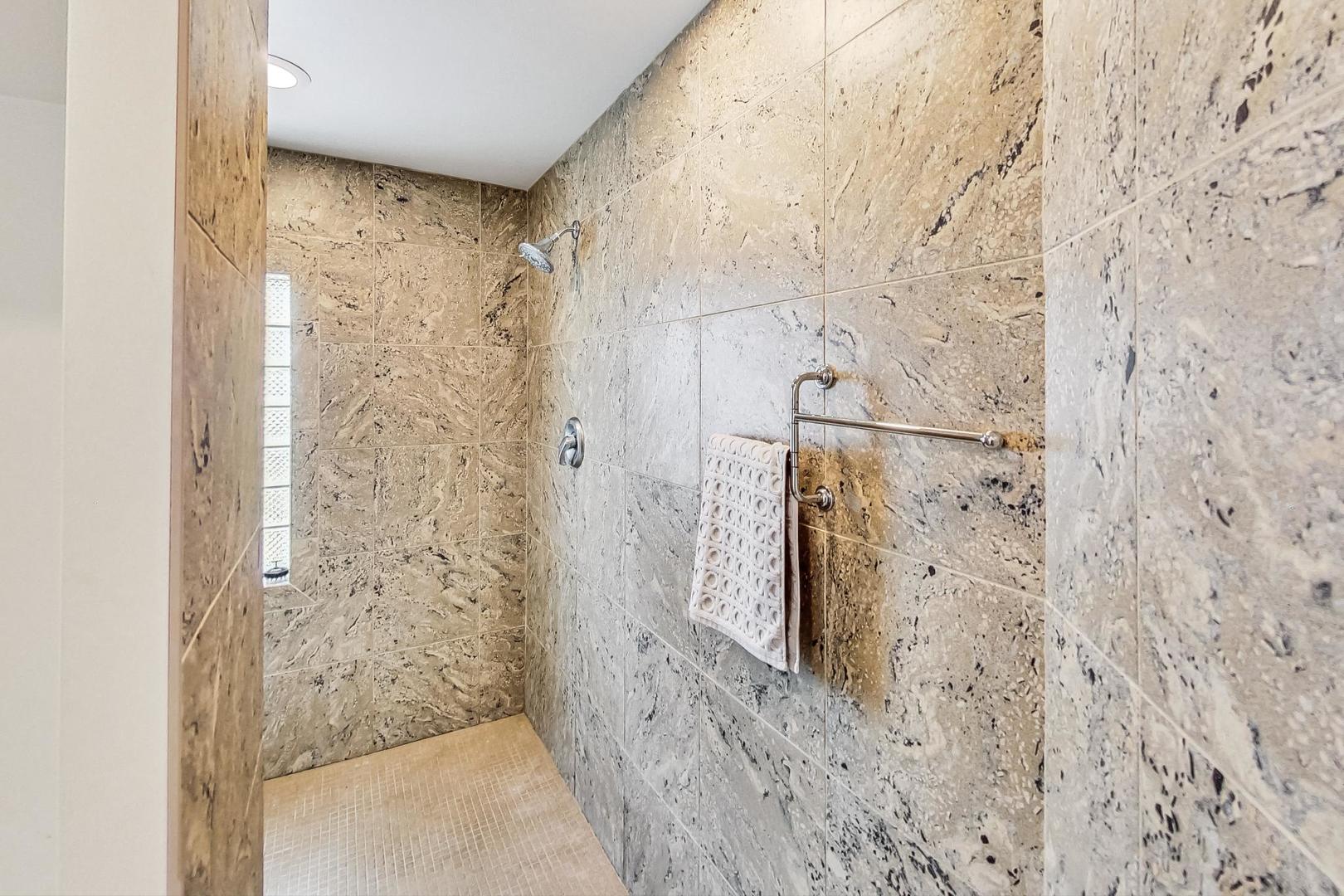 Stone-tiled walk-in shower with a glass-block window and towel bar.