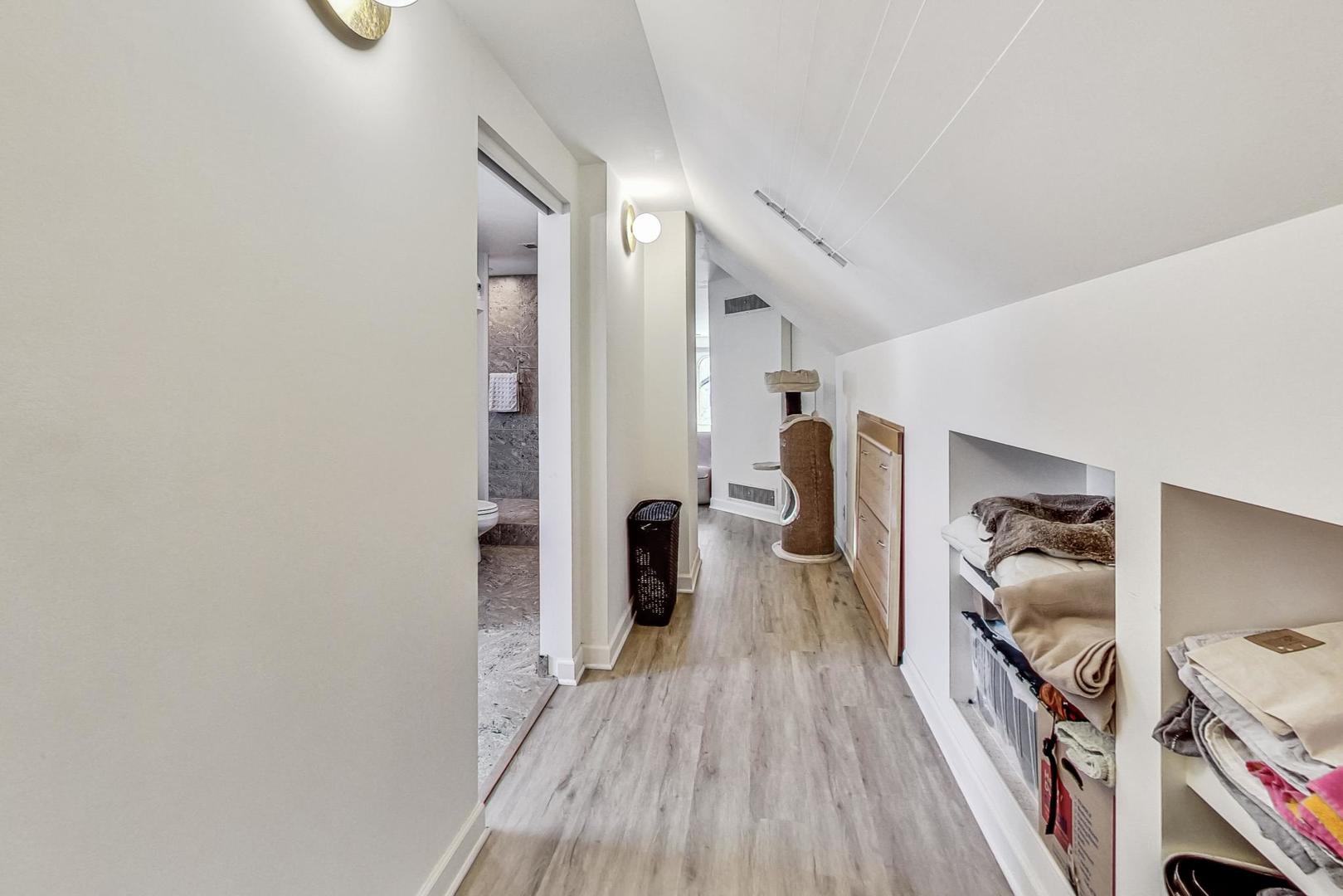 Upper-floor hallway with sloped ceiling, built-in storage cubbies, and gray wood-look flooring.
