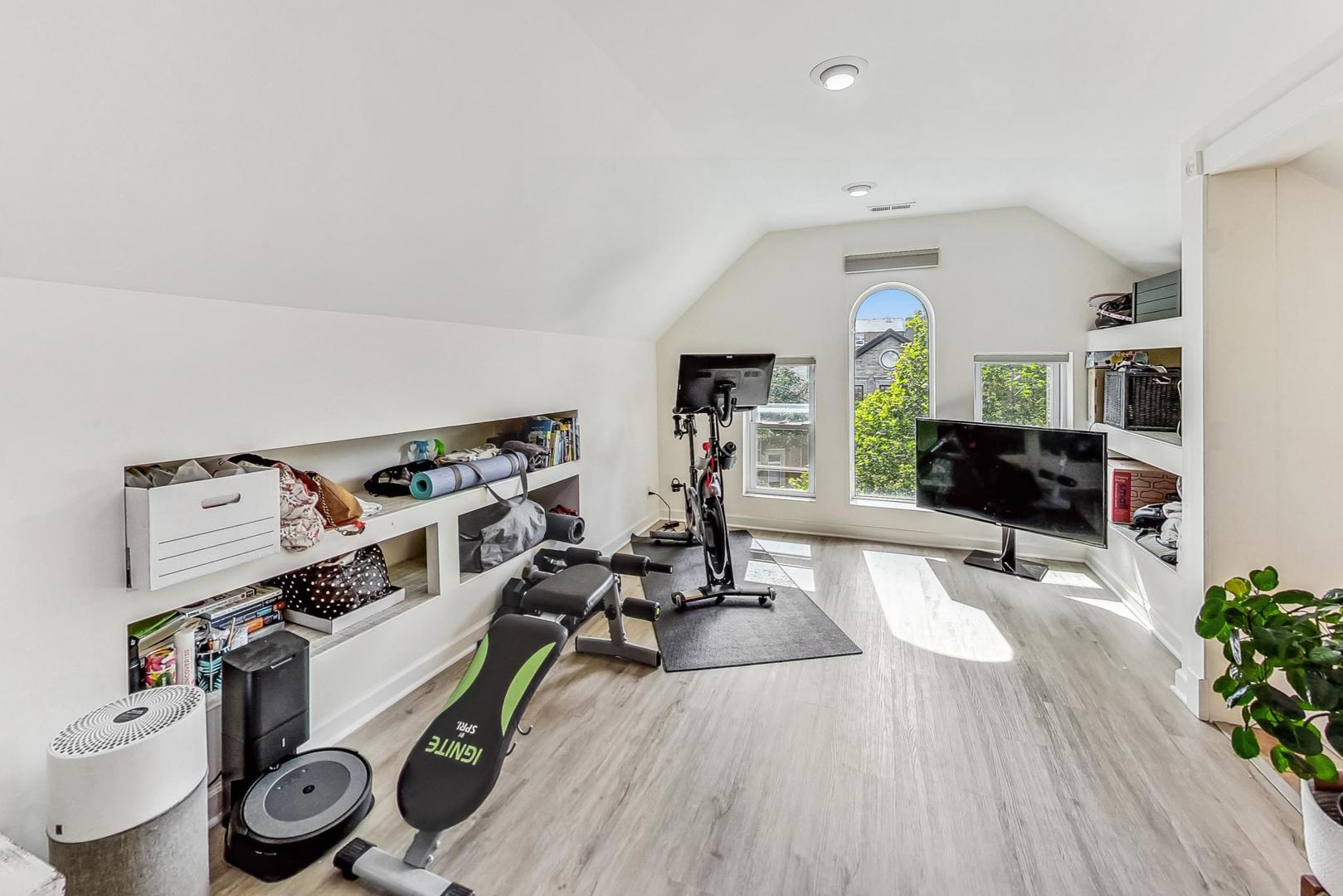 Attic exercise room with workout equipment, built-in shelves, and an arched window.