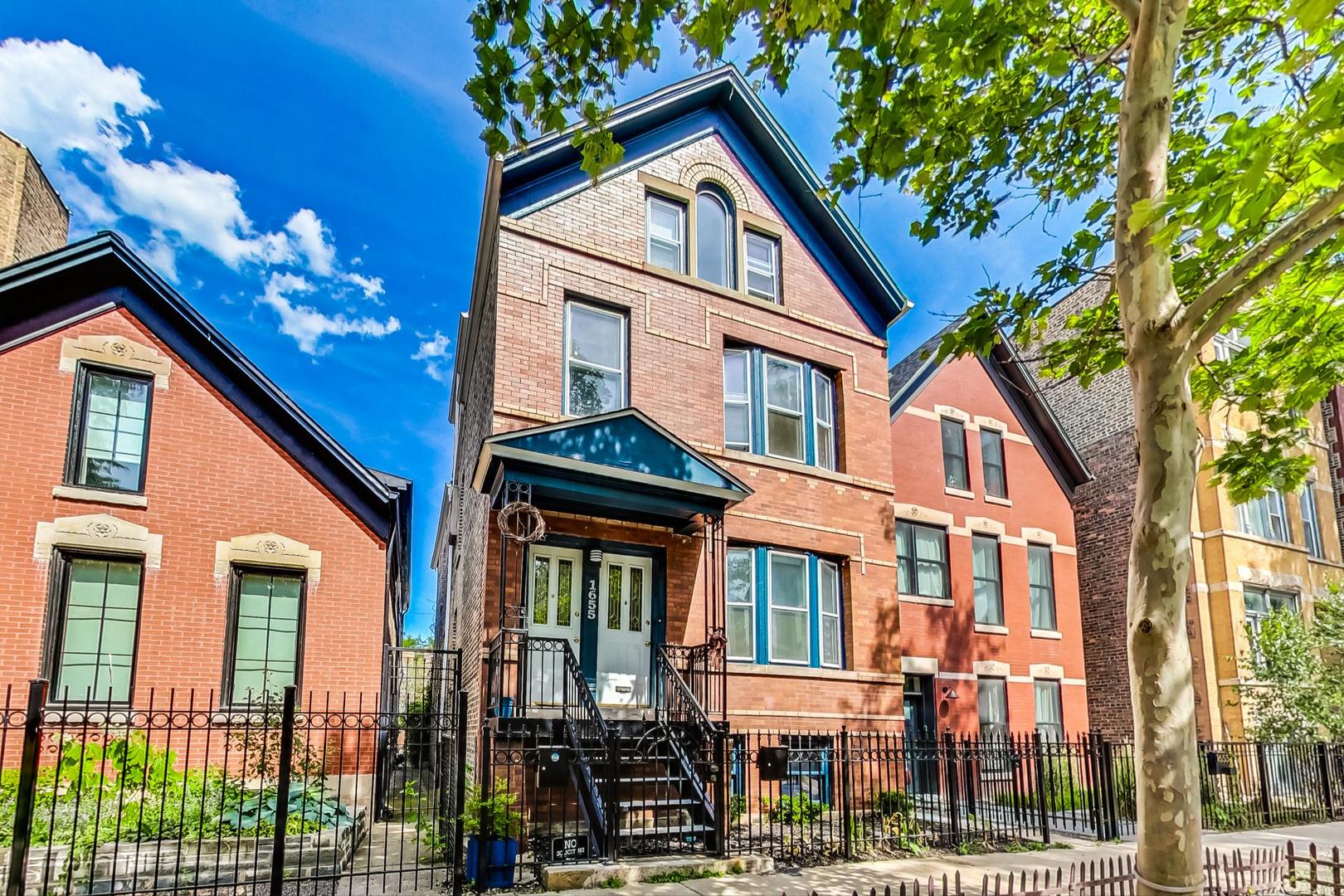 Red-brick three-story home with a steep gabled roof, dark trim, and fenced front steps.