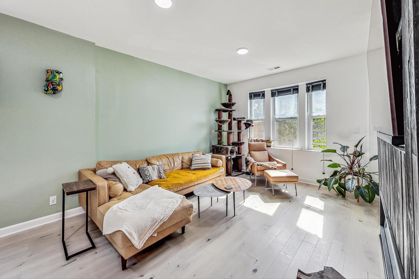 Living room with a tan leather sectional, mustard throw, large windows, and a tall cat tree.