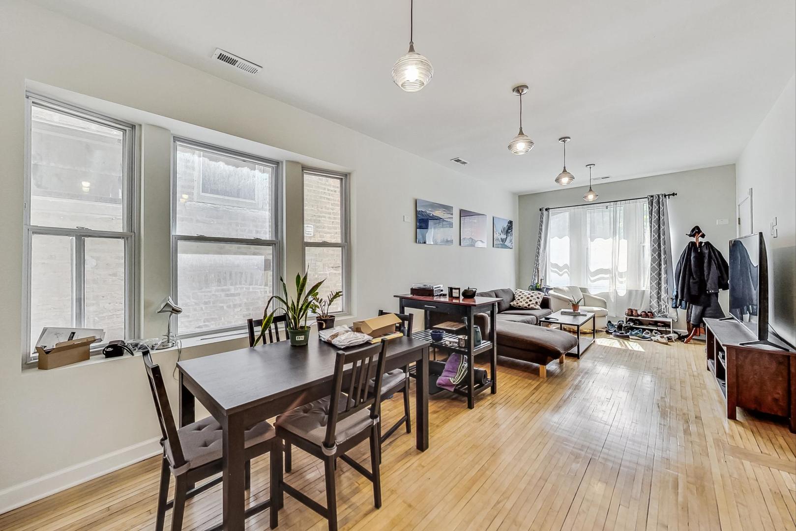 Open-plan living and dining room with tall windows, hardwood floors, and a gray sectional sofa.