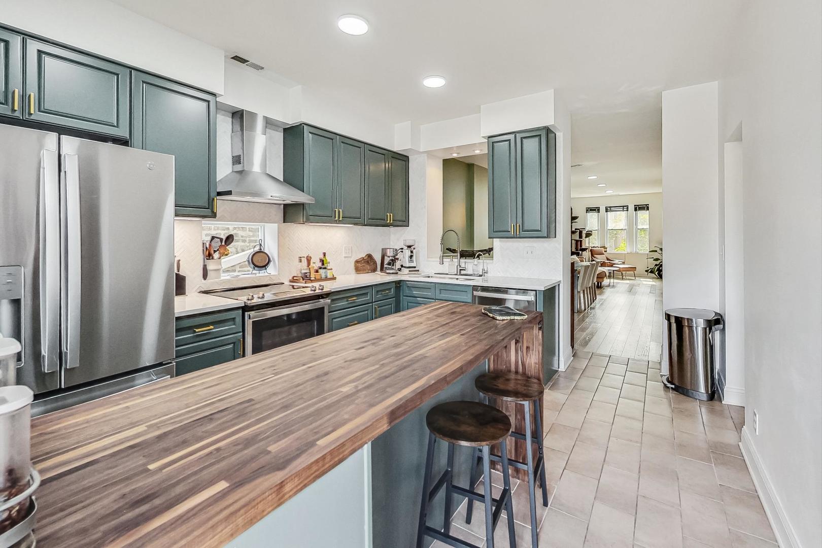 Kitchen with dark green cabinets, stainless steel appliances, and a long wood-topped island with stools.