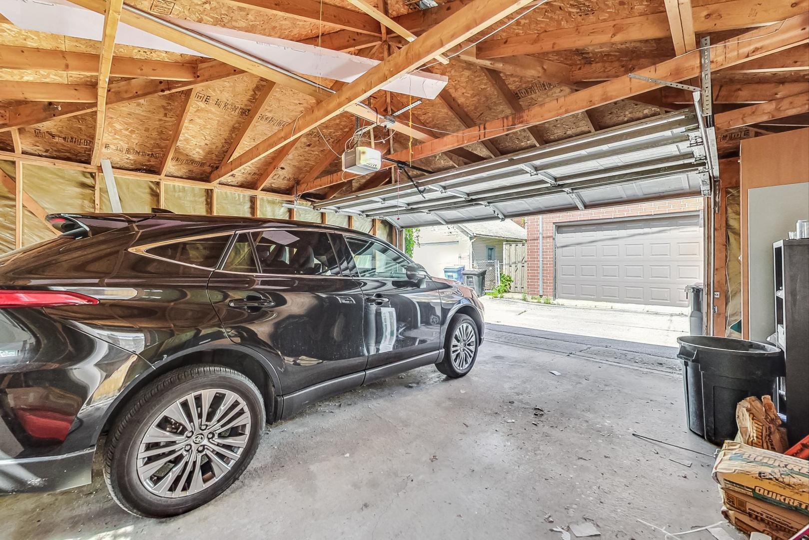 Garage with exposed roof framing and an open overhead door, with a black SUV parked inside.