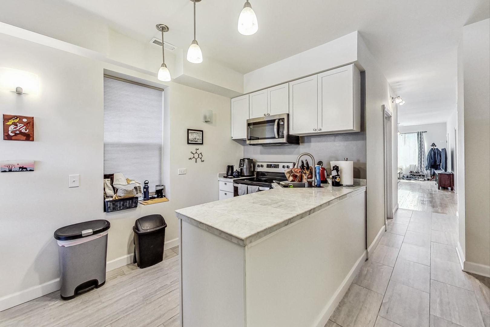 Kitchen with white cabinets, stainless appliances, and a long marble-look island.