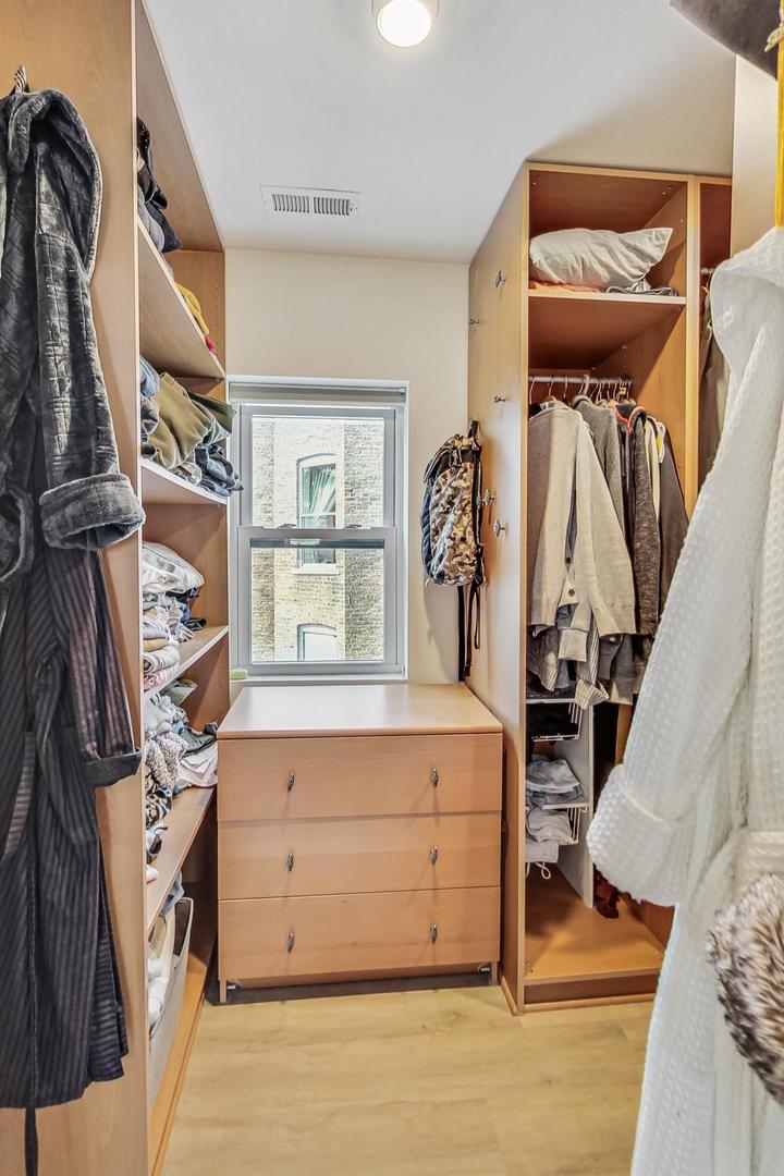 Walk-in closet with built-in wood shelving, a central dresser, and a window.