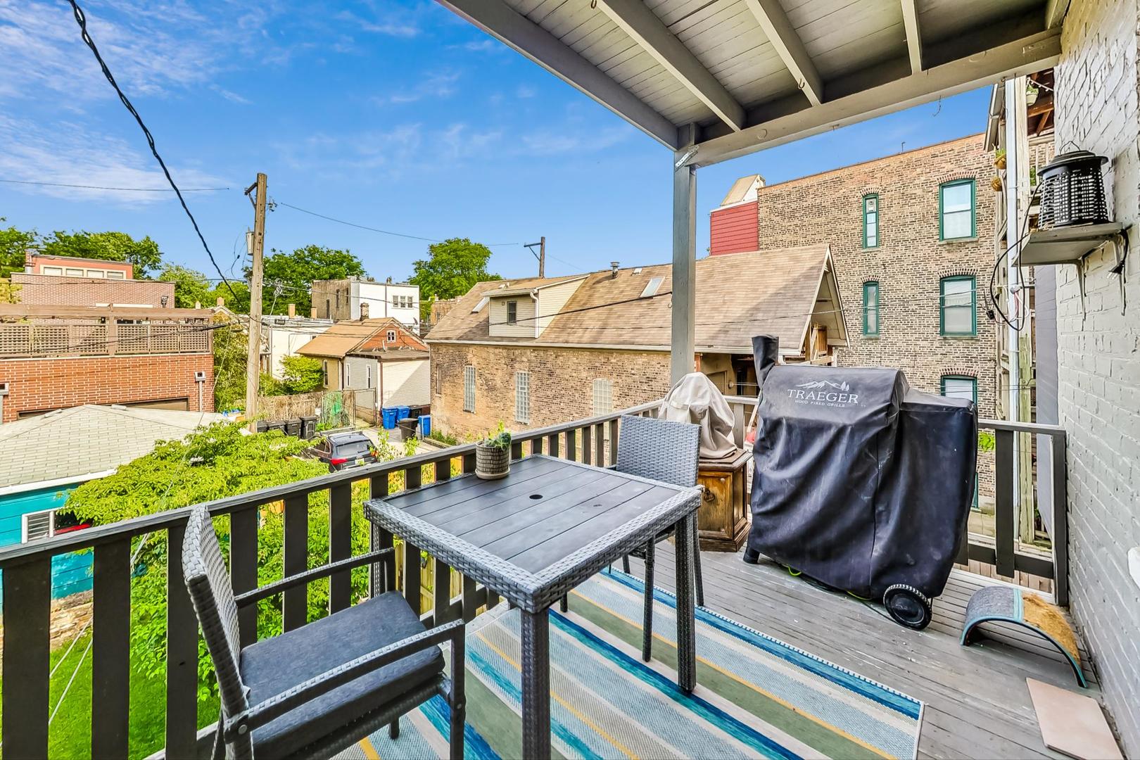 Rooftop deck with a dining set and covered grill overlooking neighboring buildings and green yards.