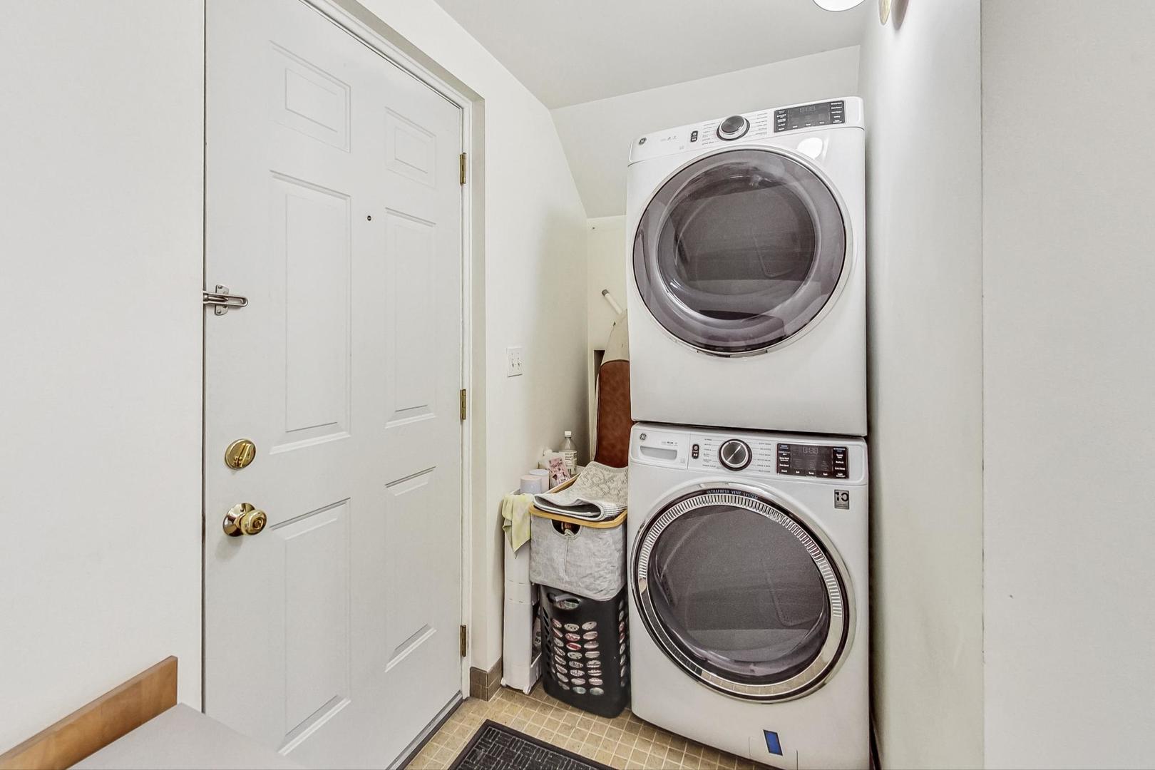 Laundry area with stacked front-loading washer and dryer beside a paneled door.
