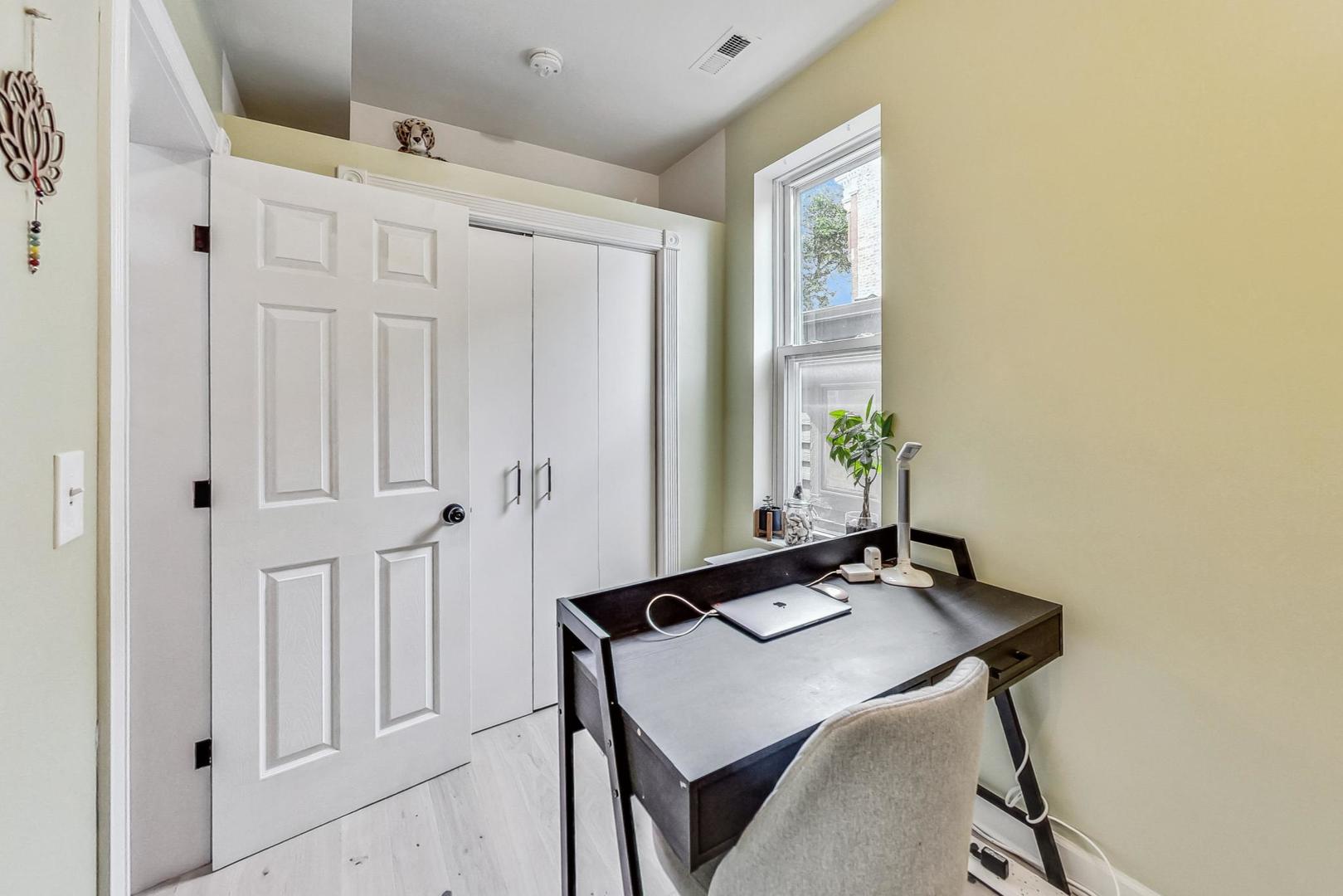 Home office with a dark desk by a window and white paneled doors.