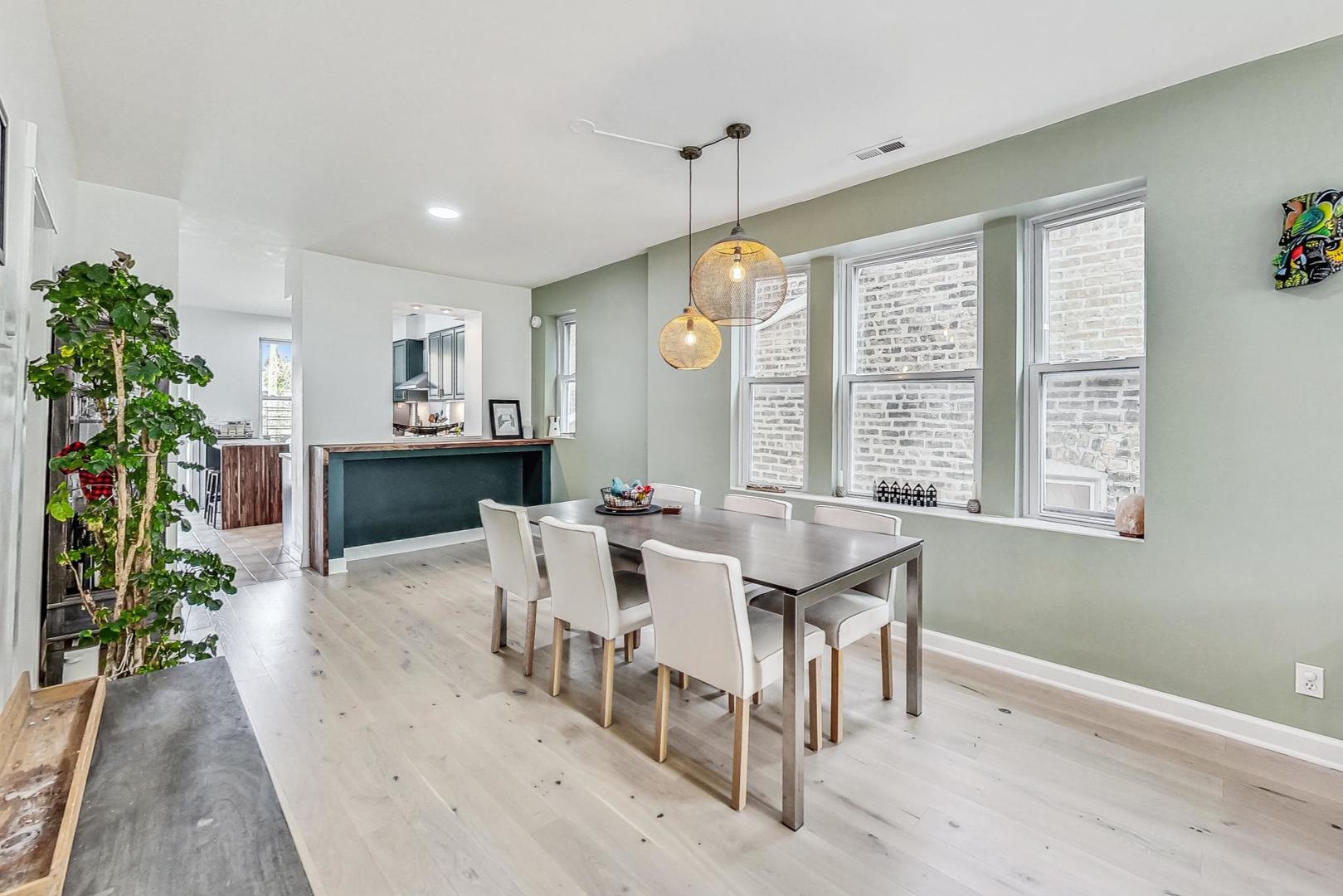 Dining room with a long table, woven pendant lights, pale wood floors, and large windows.