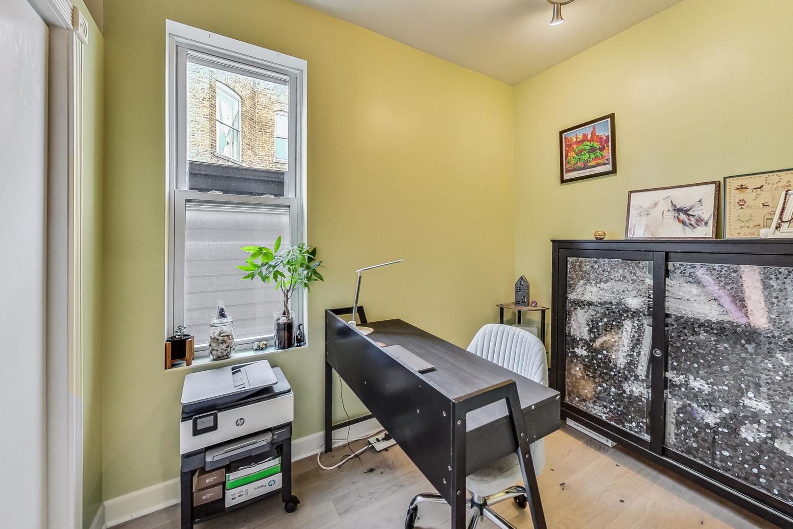 Home office with a dark desk, tall window, printer, and glass-front cabinet.