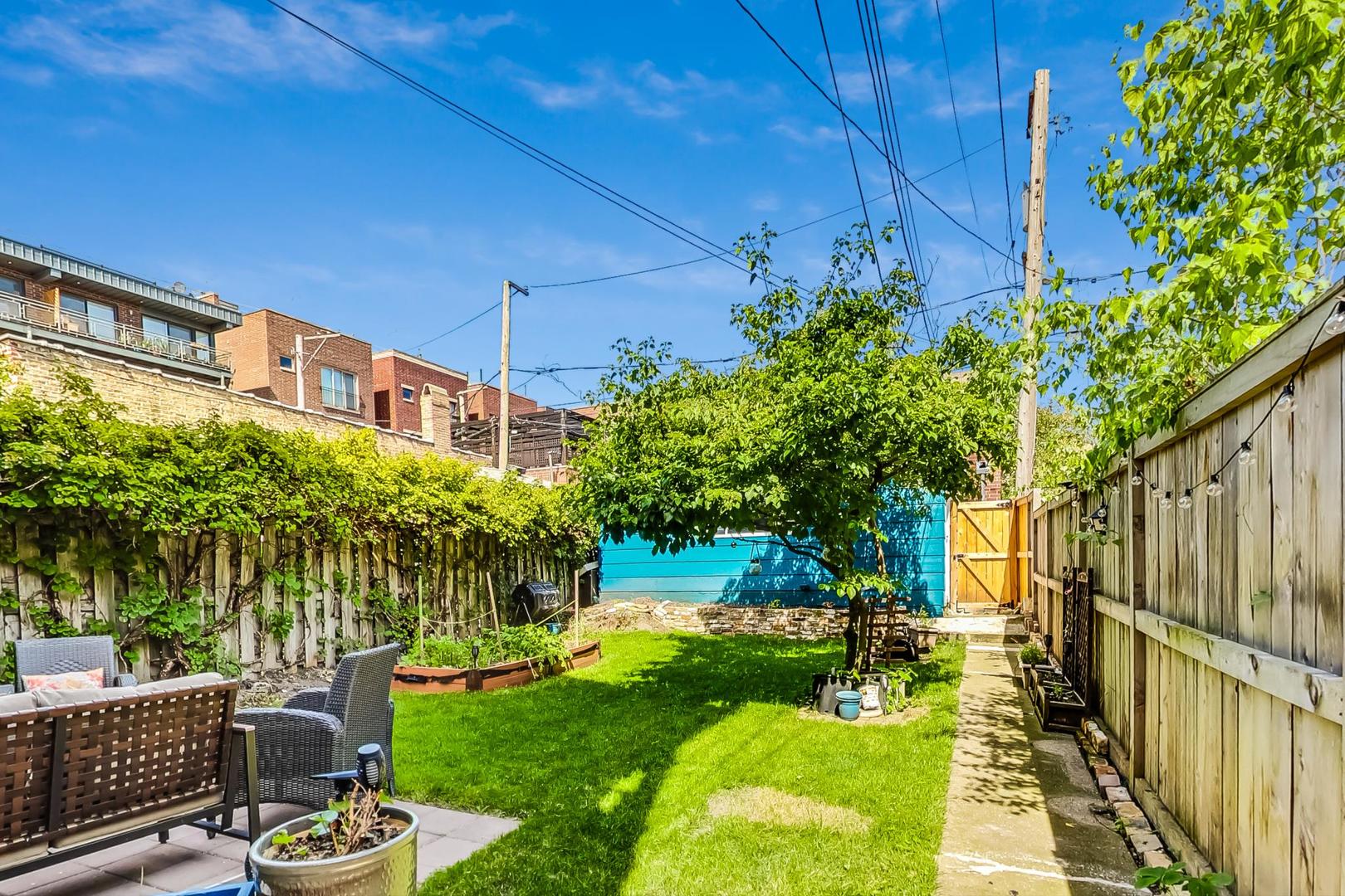 Backyard with a lawn, patio seating, raised garden beds, and a shade tree.