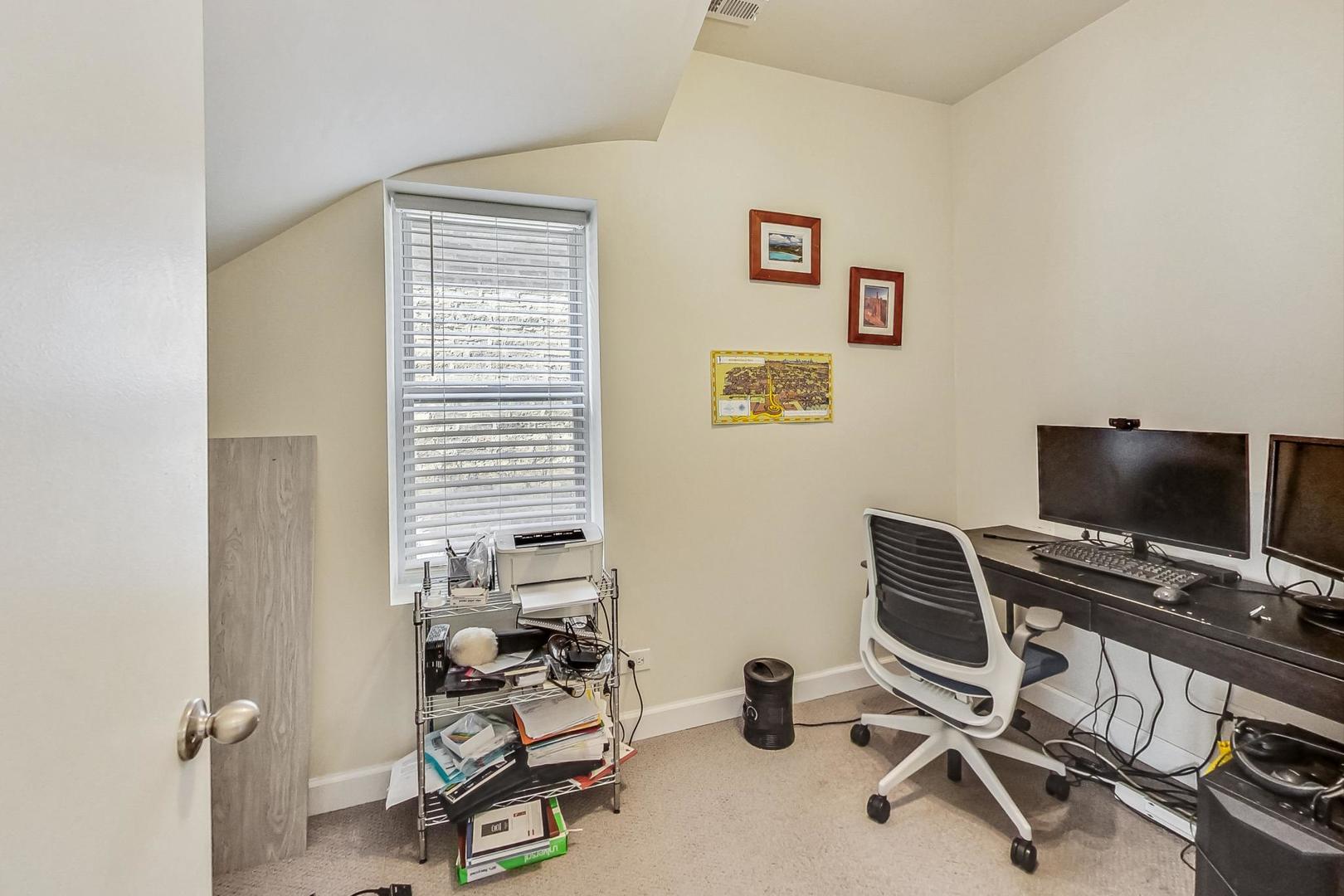 Home office with a sloped ceiling, window blinds, dual monitors, and a printer cart.